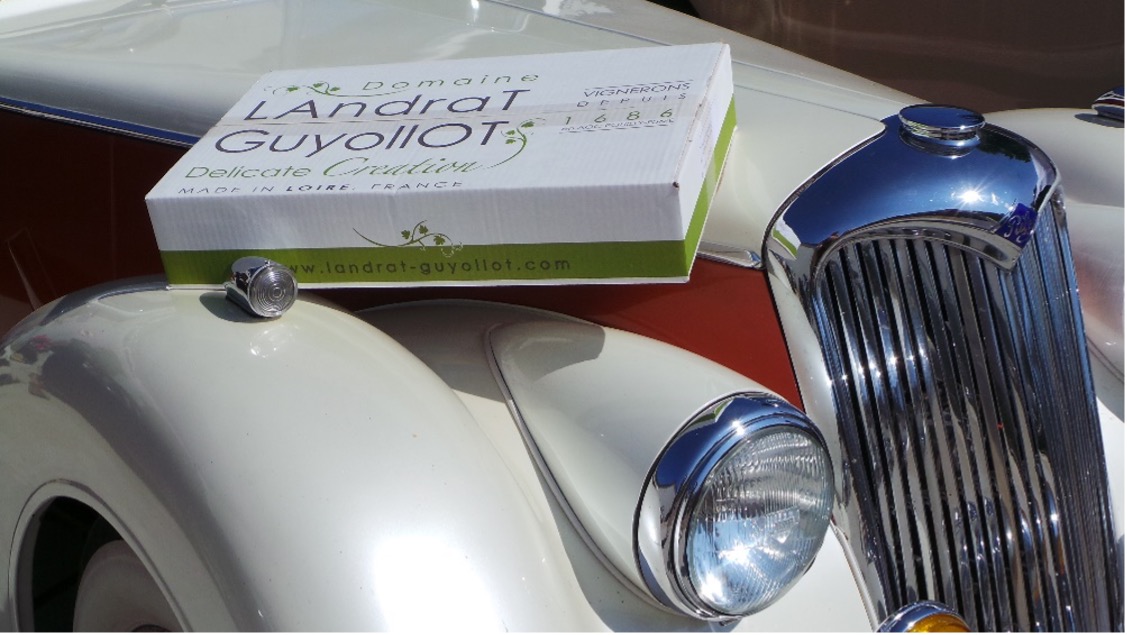 Accueil d'un Club de Voitures Anciennes Un carton de bouteilles du domaine posé sur une voiture ancienne